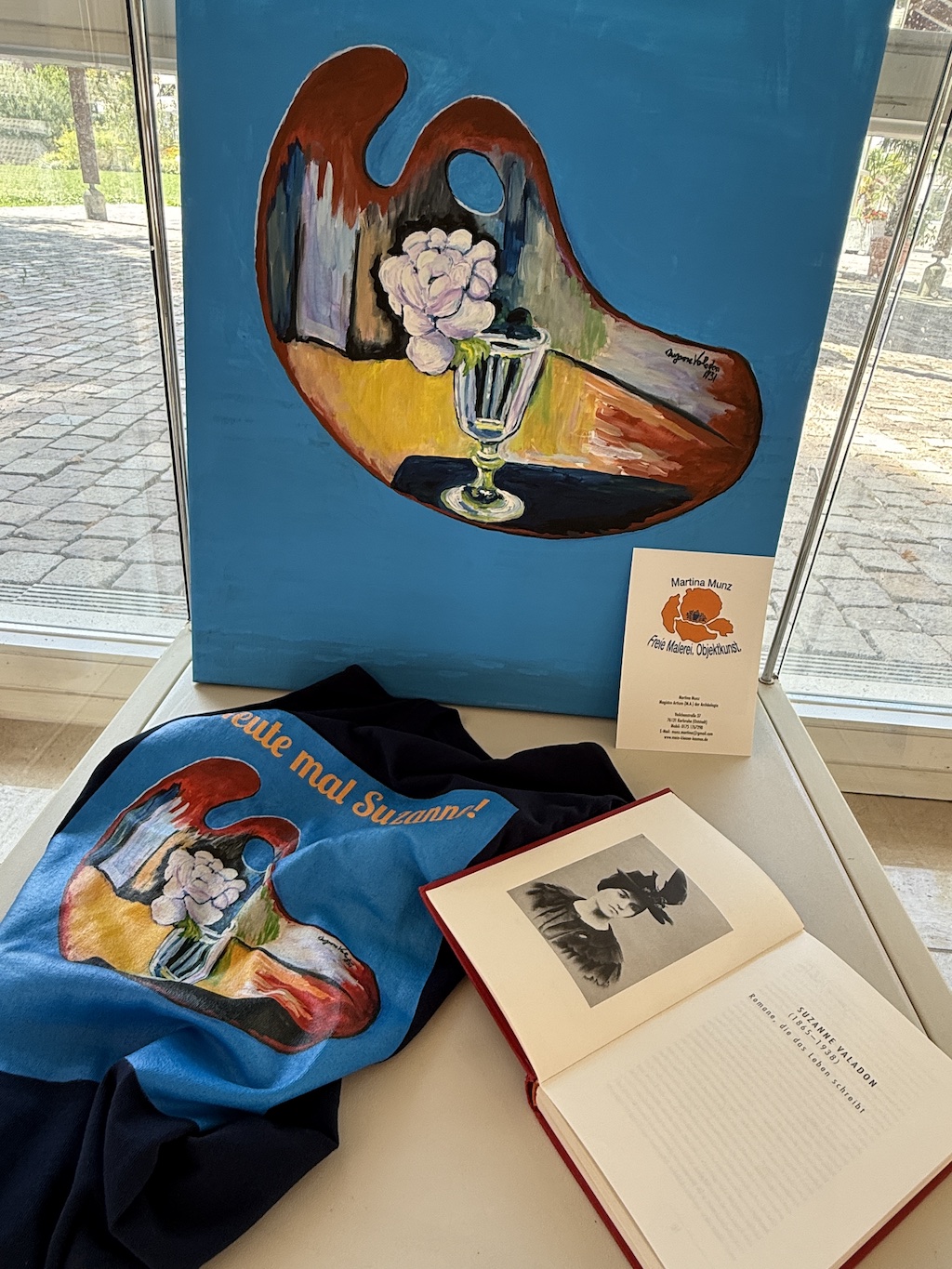 Das Bild zeigt eine Vitrine mit T-Shirt, Gemälde und ein Buch über Valadon.